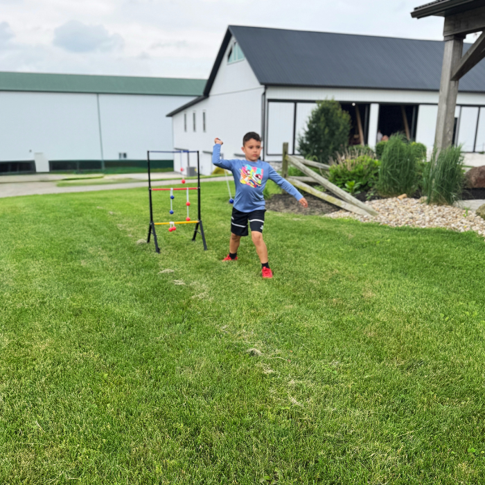 Child playing with ladder ball in a grassy area with a building in the background