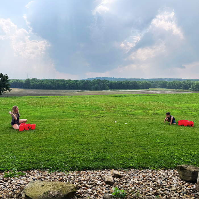 Two people sitting on a grassy field with red bags, under a blue sky with clouds.