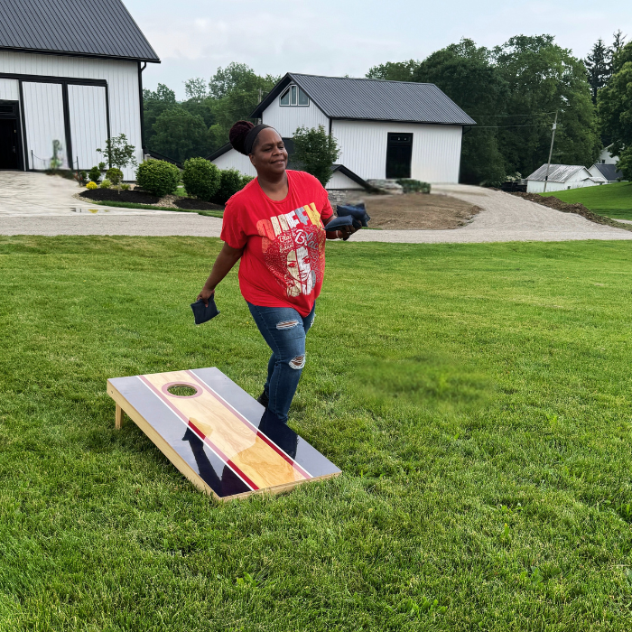 Person playing cornhole in a backyard with houses and trees in the background
