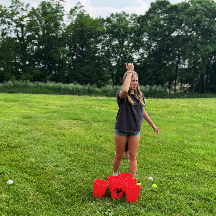 Person playing a game with red buckets and white balls on a grassy field