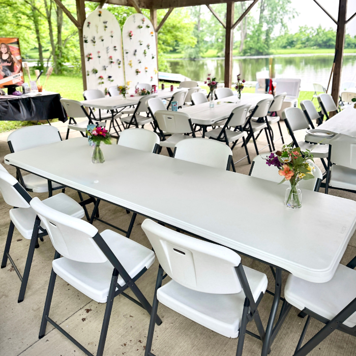 Outdoor event setup with white tables and chairs by a lake.