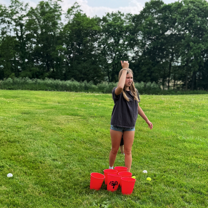 Person playing a game with red buckets and white balls on a grassy field