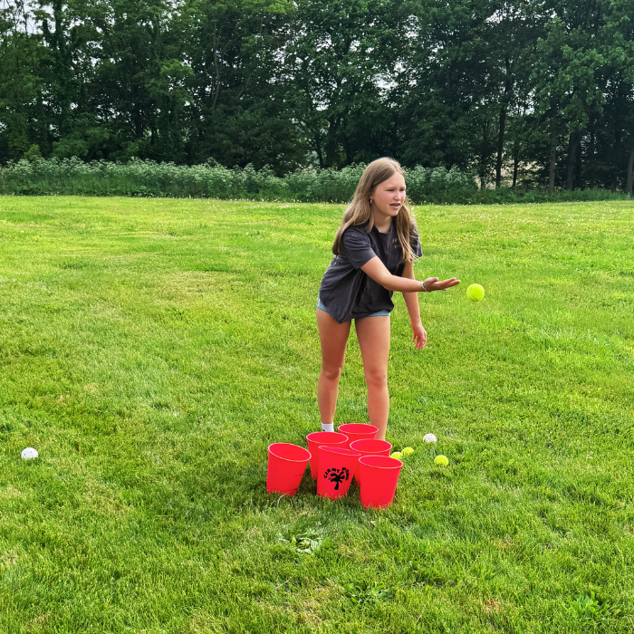 Girl playing a game with red cups and balls on a grassy field