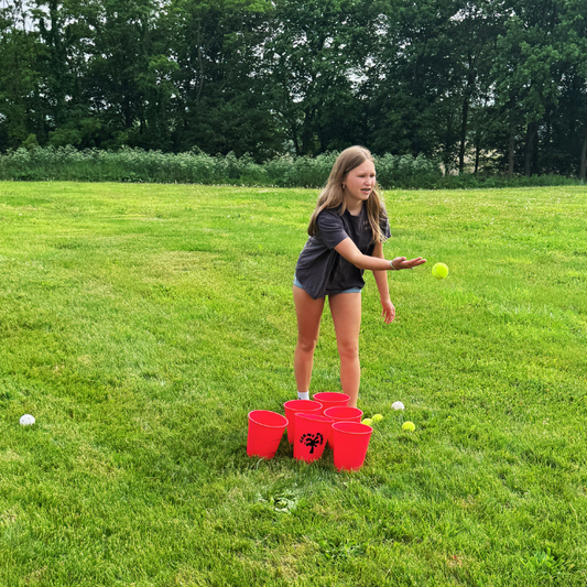 Girl playing a game with red cups and balls on a grassy field